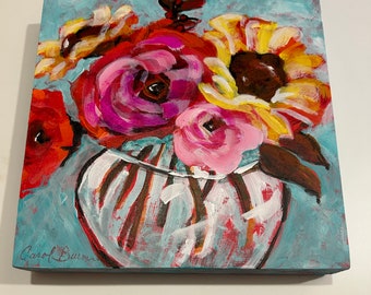 May include: A painting of a colorful floral arrangement in a white vase with brown, red, pink, yellow, and white flowers. The background is a light blue color. The artist's signature, "Carol Burr", is in the bottom left corner.