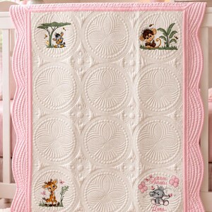 May include: A white baby quilt with a scalloped pink border featuring quilted circular patterns and embroidered animal motifs including a zebra, monkey, giraffe, and an elephant holding balloons with the name Lara printed in cursive script.