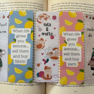 May include: Five decorative bookmarks with different designs. One shows a koala, another has lemons and the text "When life gives you lemons... sell them and buy fabric." Other bookmarks feature cats, yarn, and penguins.