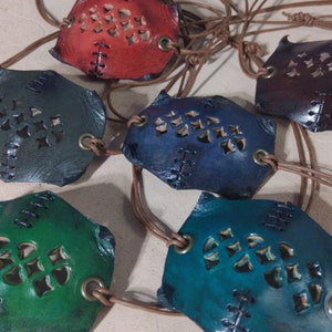 Può includere: Cinque parches per occhi in pelle con intricati ritagli e cinturini in pelle marrone. I parches per occhi sono di vari colori, tra cui rosso, blu, verde e turchese.