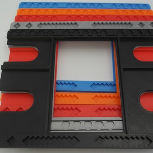 May include: A black plastic frame with a series of colorful plastic inserts. The inserts are layered and feature different patterns, including diamonds, zigzags, and waves. The frame is designed to hold a picture or other artwork.