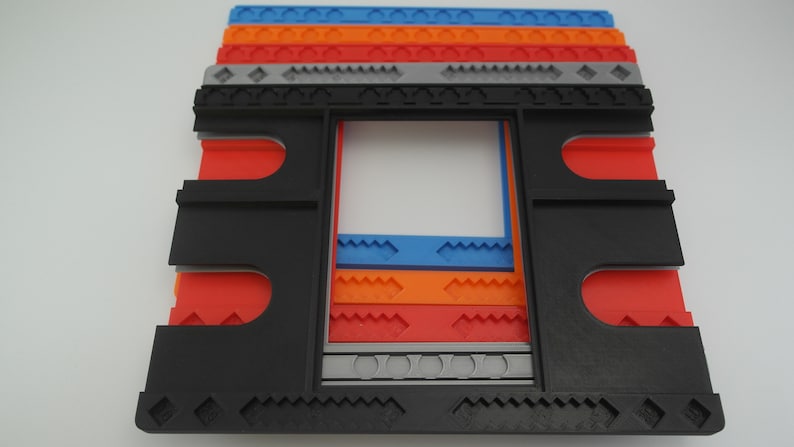 May include: A black plastic frame with a series of colorful plastic inserts. The inserts are layered and feature different patterns, including diamonds, zigzags, and waves. The frame is designed to hold a picture or other artwork.