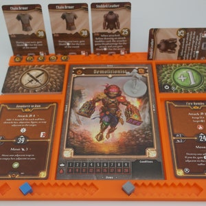 May include: An orange game board with cards for a tabletop role-playing game. The cards show a character called "Demolitionist" with a red helmet and a character called "Fire Bombs" with a red and brown design. The board has a number of spaces for cards and tokens.