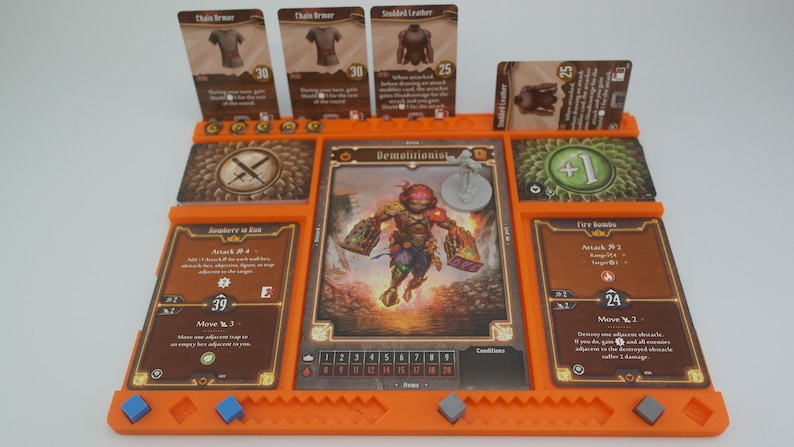 May include: An orange game board with cards for a tabletop role-playing game. The cards show a character called "Demolitionist" with a red helmet and a character called "Fire Bombs" with a red and brown design. The board has a number of spaces for cards and tokens.