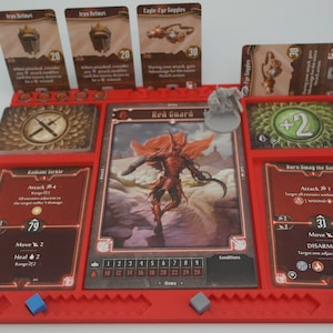 May include: A red plastic game board with compartments for cards and miniatures. The board has a red guard character card with a red demon figure, and other cards with text like "Attack 2d4" and "Move 2".