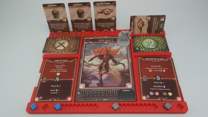 May include: A red plastic game board with compartments for cards and miniatures. The board has a red guard character card with a red demon figure, and other cards with text like "Attack 2d4" and "Move 2".