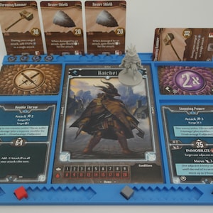 May include: A blue game board with a miniature figure of a character named "Hatchet" and cards with the text "Throwing Hammer", "Bear Shield", "Stepping Power", "Private Terror", and "2x".