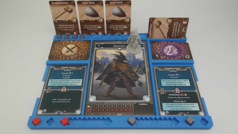 May include: A blue game board with a miniature figure of a character named "Hatchet" and cards with the text "Throwing Hammer", "Bear Shield", "Stepping Power", "Private Terror", and "2x".