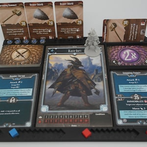 May include: A tabletop game setup with a character card for "Hatchet" and a miniature figure. The character card has a health tracker and a list of conditions. The player has a variety of cards in their hand, including "Double Throw", "Throwing Hammer", "Razor Shield", and "Stepping Point".