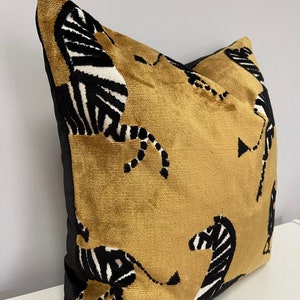 May include: A mustard yellow velvet pillow with a black and white zebra print. The pillow has a black velvet border.