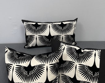 May include: Decorative throw pillows with a black and white crane pattern. The pillows have a black border and a cream-colored background. The crane design is repeated across the surface of the pillows. The pillows are arranged on a gray sofa.
