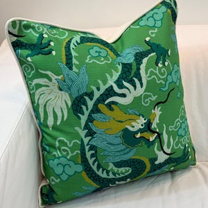 May include: A square throw pillow featuring a vibrant green background with a repeating dragon motif in shades of teal, dark green, and yellow. The design includes stylized clouds and dragon claws, finished with a solid white piped edge trim.