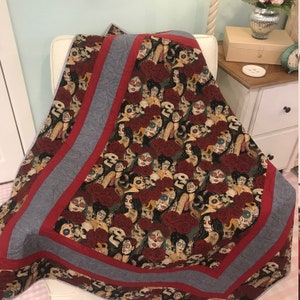 May include: A red and gray quilt with a pattern of sugar skulls and roses. The quilt is made of cotton fabric and is perfect for adding a touch of spooky elegance to any room.