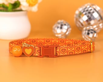 May include: Orange cat collar with a heart pattern and a gold heart charm. The collar has a red buckle and a small bell.