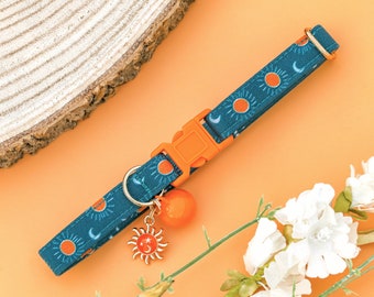 Puede incluir: Un collar para gato azul y naranja con un diseño de sol y luna. El collar tiene una hebilla dorada y un dije colgante con un diseño de sol y luna.