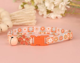 May include: A pink and orange floral patterned cat collar with an orange buckle and a pink bell with a gold flower charm.