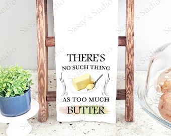 Könnte beinhalten: Ein weißes Küchentuch mit einer schwarz-weißen Grafik, auf der "Es gibt kein solches Ding wie zu viel Butter" steht. Die Grafik zeigt eine Stange Butter und ein Buttermesser. Das Tuch hängt an einer Holzleiter.