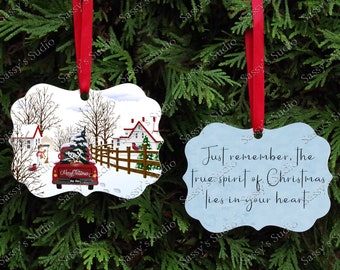 Op de afbeelding: Twee kerstversieringen. Een ornament is wit met een rode vrachtwagen die een kerstboom vervoert. De andere versiering is blauw met de tekst "Just remember, The true spirit of Christmas lies in your heart."