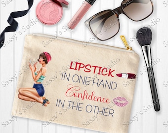 May include: A beige canvas makeup bag with a red and blue graphic that says "Lipstick in one hand, confidence in the other". The graphic includes a woman with red hair and a red lipstick, a red lipstick tube, and a pink glitter lip.