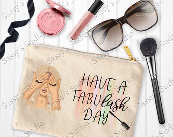 May include: A beige canvas makeup bag with a zipper closure. The bag features a colourful abstract design and the text "HAVE A FABUlash DAY". A woman with blonde hair is illustrated on the bag with her hands covering her eyes.