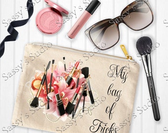 May include: A beige canvas makeup bag with a zipper closure. The bag features a design of pink lilies and makeup brushes. The text "My bag of Tricks" is printed on the bag.