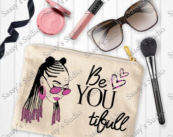 May include: A beige canvas makeup bag featuring a black and pink illustration of a woman with braids and sunglasses. The text "Be You tifull" is printed in black on the bag.