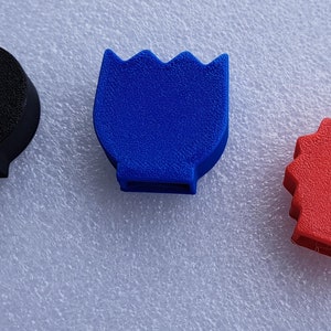 May include: Three 3D printed plastic shapes: a black round shape, a blue flower-shaped object, and a red star-shaped object.