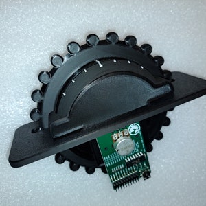 May include: A black 3D printed rotary encoder with a green circuit board attached. The circuit board has a small potentiometer and a white logo that says "STM32".