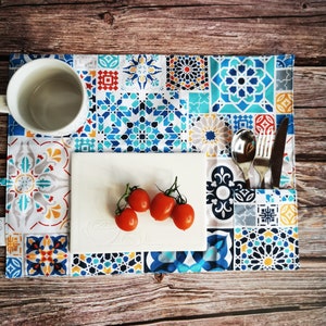 Könnte beinhalten: Ein rechteckiger Tischset mit einem lebendigen, geometrischen Fliesenmuster in Blau-, Weiß- und Gelbtönen. Eine weiße Tasse, ein weißer Teller mit Tomaten und Besteck sind auf dem Tischset angeordnet.
