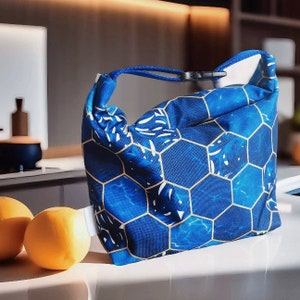 Op de afbeelding: Een blauwe en gouden lunchtas met een geometrisch patroon. De tas heeft een ritssluiting en een bovenste handvat.