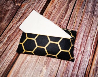 Può includere: Un porta fazzoletti in tessuto nero e oro con motivo a nido d'ape con un fazzoletto bianco all'interno.