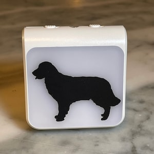 May include: A white night light with a black silhouette of a dog. The night light has two buttons on the top.