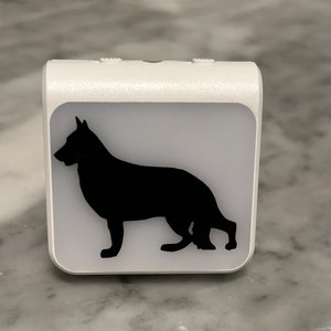 May include: A white night light with a black silhouette of a German Shepherd dog.