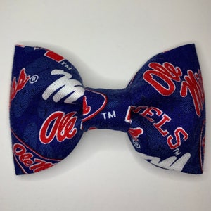 May include: A blue bow tie with a white and red pattern featuring the text "Ole Miss Rebels" repeated throughout.
