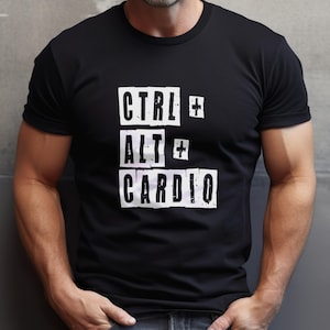 May include: A black short-sleeved t-shirt featuring white distressed-style text printed on the chest. The graphic displays the words CTRL, ALT, and CARDIO stacked vertically, each enclosed in a white rectangular box with plus signs between them.