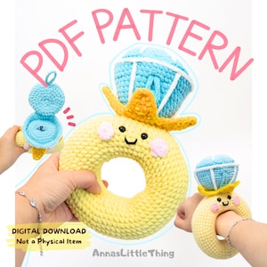 Op de afbeelding: Een PDF-patroon voor een gehaakte babyrammelaar in de vorm van een gele donut met een lachend gezicht, een blauwe diamantvormige kroon en een gele hoed. De tekst "PDF PATTERN" staat in roze boven de rammelaar. De woorden "DIGITAL DOWNLOAD Not a Physical Item" zijn ook zichtbaar.