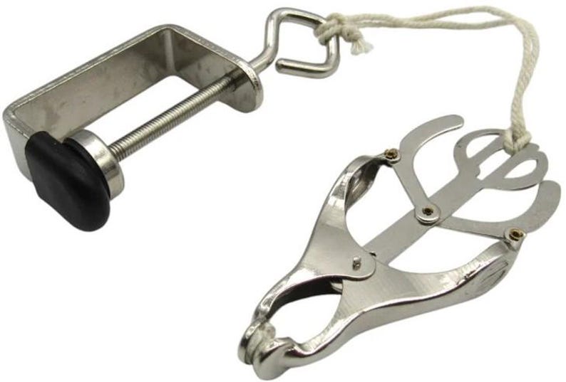 May include: A silver-colored clamp with a black knob and a hinged, scissor-like mechanism. A white cord connects the clamp to the scissor-like device. The device is designed to hold objects.