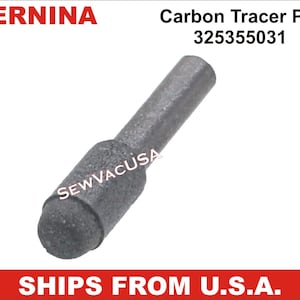 May include: A gray carbon tracer pin with the text "Carbon Tracer Pin 325355031" and the brand name "BERNINA". The pin has a cylindrical body and a rounded tip. The text "SEW VACUSA" is also visible.
