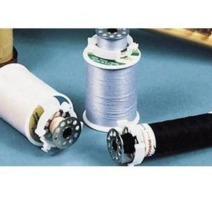 May include: Three spools of thread in the image. One is white, one is silver, and one is black. The spools are on a blue surface. The spools are for sewing and crafting.