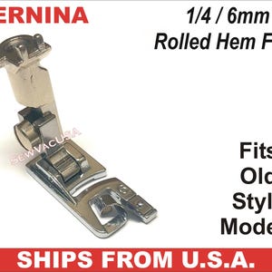 May include: A silver-colored Bernina rolled hem foot for sewing machines. The foot is labeled "1/4 / 6mm" and "Fits Old Style Models". The brand name "BERNINA" is visible at the top. The text "SEWVACUSA" is also visible.