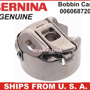 May include: A silver bobbin case for a Bernina sewing machine. The case has a small lever on the side and the text "SEWVACUSA" is printed on the case.