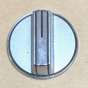 May include: A circular silver-colored control knob with a metallic finish. The knob features a raised rectangular center section that runs vertically across the face, marked with a thin, dark vertical line to indicate the current setting position.