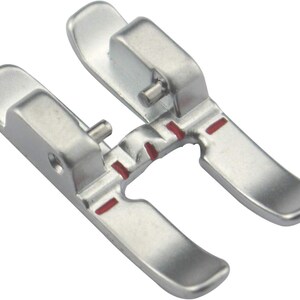 May include: A silver sewing machine foot with a curved design. The foot has a rectangular top with a pin and two curved, flat extensions. Red markings are visible on the foot.