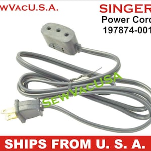 May include: A gray power cord with a three-prong plug on one end and a two-prong plug on the other end. The cord is coiled and the text "SINGER Power Cord 197874-001" is visible.