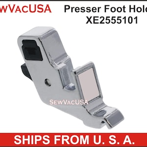 May include: Silver sewing machine presser foot holder with a black plastic piece. The holder has the text "SEWVACUSA" printed on it. The part number "XE2555101" is printed above the image. The text "SHIPS FROM U.S.A." is printed below the image.