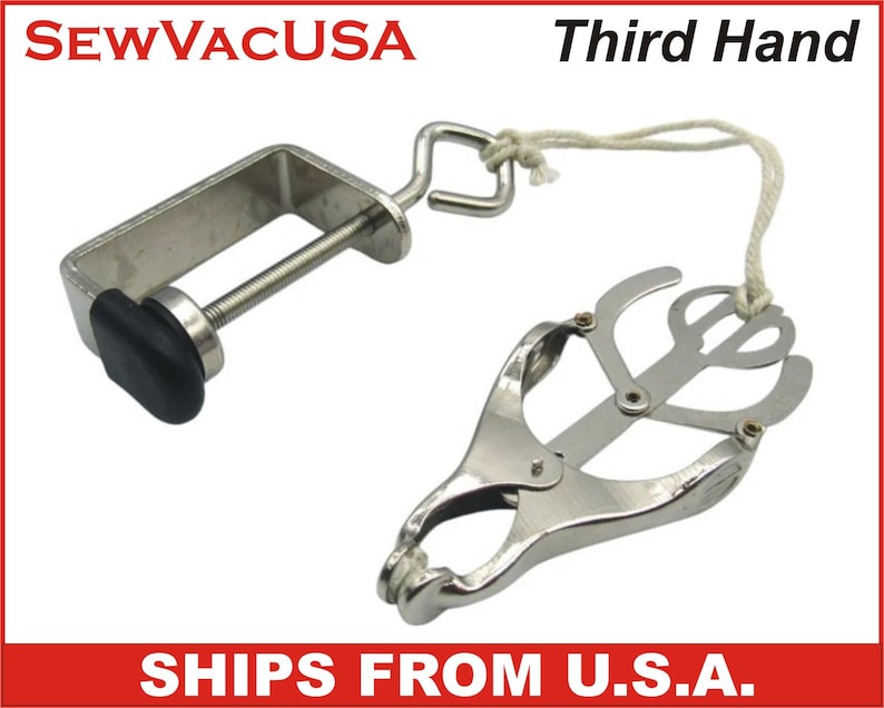 May include: A silver-colored Third Hand tool with a clamp and adjustable jaws. The clamp has a black rubber grip. The tool is connected to a string. The text "Third Hand" is visible.