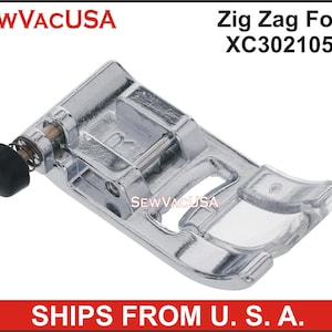 May include: A silver-toned zig zag foot for a sewing machine. The foot has a clear plastic guide and a spring-loaded adjustment knob. The foot is labeled "Zig Zag Foot XC3021051".