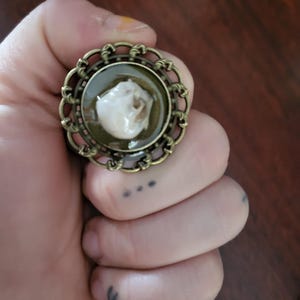 May include: A ring with a bronze filigree setting and a glass dome containing a small white skull.