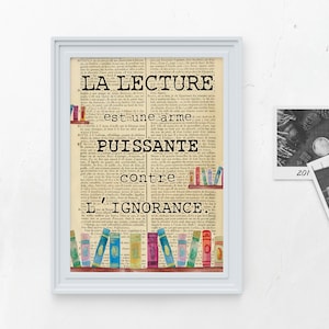 Peut inclure: Une impression encadrée avec un fond de page de livre vintage présentant le texte "LA LECTURE est une arme PUISSANTE contre L'IGNORANCE." Le texte est en noir et l'arrière-plan est dans des tons de brun et de beige. Il y a des livres colorés sur une étagère en bas de l'impression.