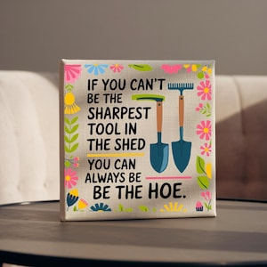 Può includere: Stampa su tela con il testo "IF YOU CAN'T BE THE SHARPEST TOOL IN THE SHED YOU CAN ALWAYS BE BE THE HOE." La stampa presenta illustrazioni di un rastrello e una pala, con un bordo floreale.